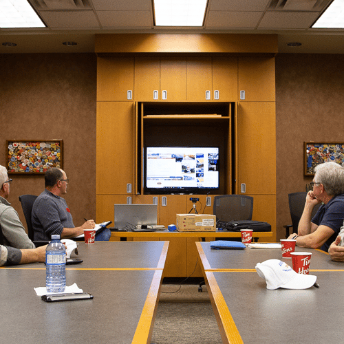 a group of men sitting at a conference table looking at a screen